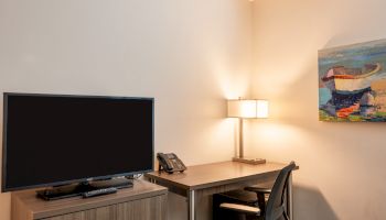 A home office setup features a TV, a desk with a phone, lamp, chair, and a colorful painting on the wall, creating a cozy workspace.