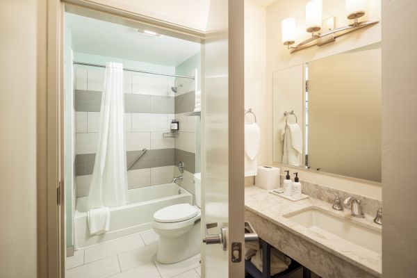 A modern bathroom with a bathtub and shower, toilet, large mirror, sink, vanity area, and well-lit setting with towels and toiletries.