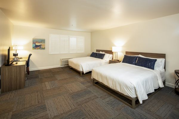 A hotel room with two neatly made beds, a desk with a chair, and two bedside lamps, featuring a neutral color palette and carpeted floor.