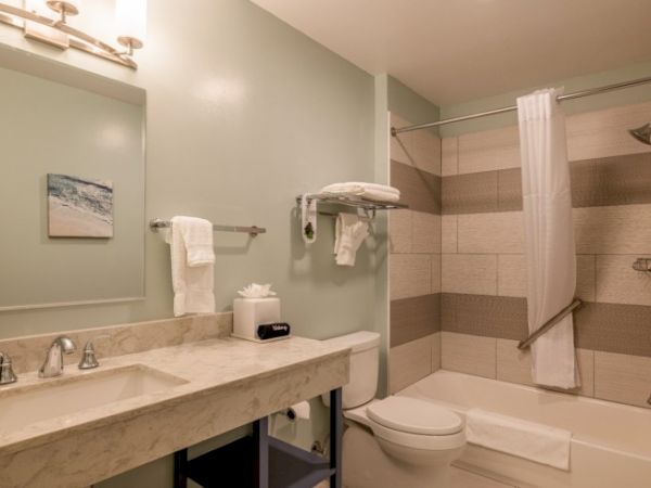 A clean bathroom with a marble sink, towels, a shower-tub combo, and modern lighting, featuring neutral tones and a small seascape artwork.