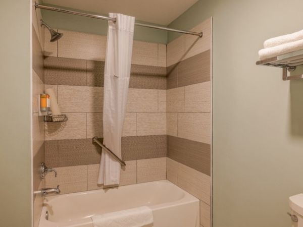 A bathroom with a bathtub, shower curtain, wall tiles, towel rack with towels, and a small shelf holding toiletries.
