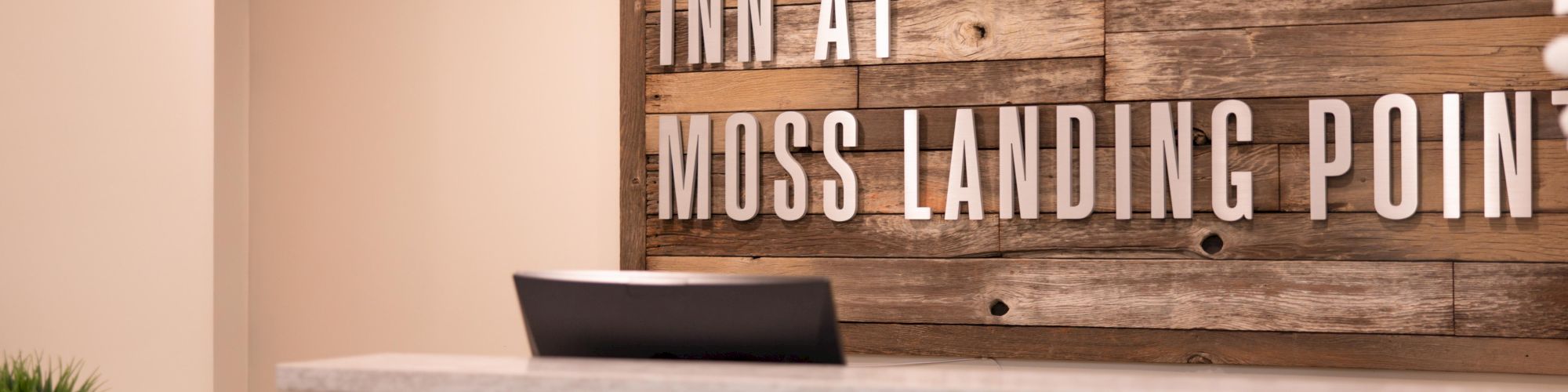 Reception area with a wooden backdrop sign reading "Inn at Moss Landing Point." A clock and small plant decorate the space.