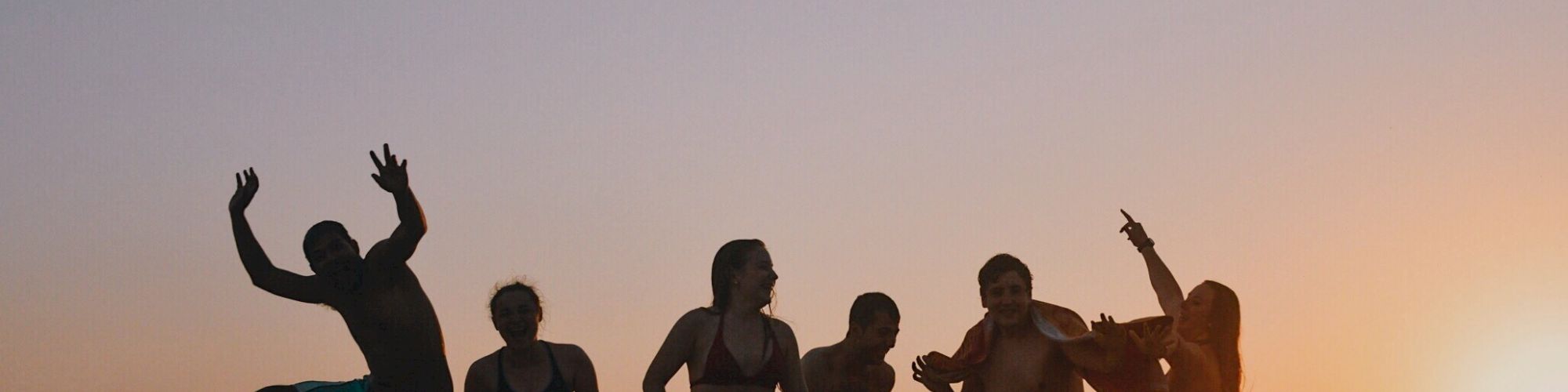 A group of people enjoying and posing on a beach during sunset, with silhouettes against the colorful evening sky.