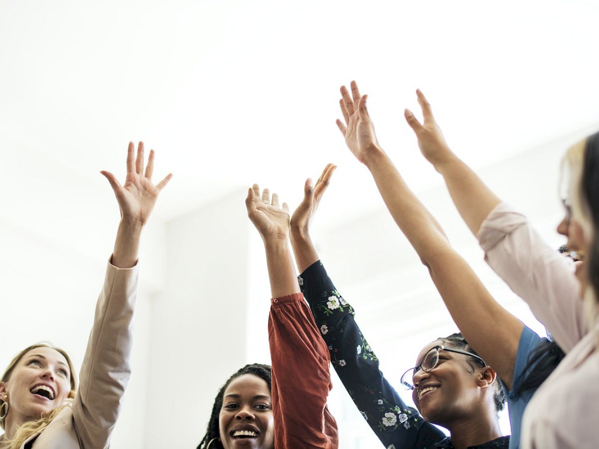 Five people are standing in a circle, smiling, and raising their hands in the air, appearing joyful and enthusiastic.