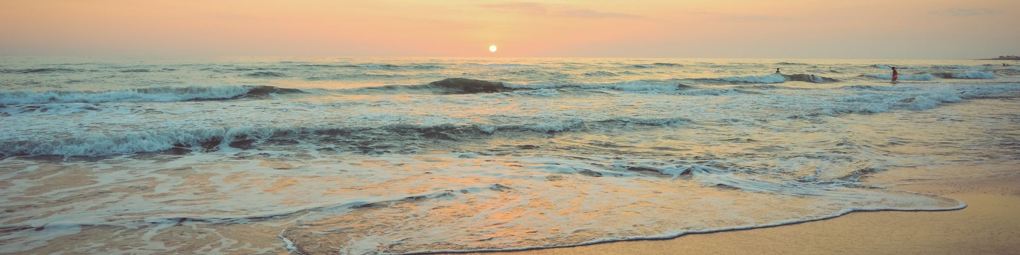 A serene beach scene with a beautiful sunset, where gentle waves roll onto the shore under a partly cloudy sky reflecting warm tones.