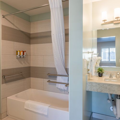 A modern bathroom with a shower, tub, vanity with mirror, and toiletries under bright lighting.