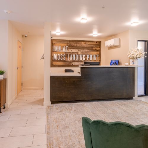 This image shows a hotel reception area with a wooden front desk and a sign reading "INN AT MOSS LANDING POINT."