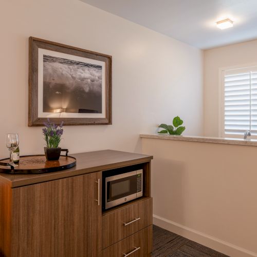 A cozy room corner with a framed photo, cabinet with a microwave, plant, and a window with shutters.