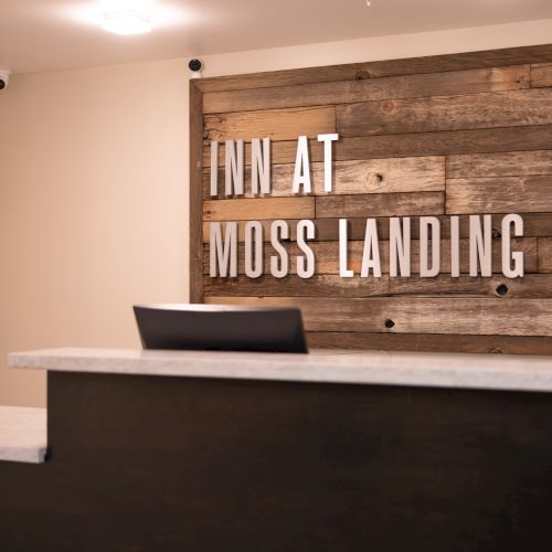 Reception area with a sign reading "INN AT MOSS LANDING POINT," a clock, and a small potted plant.