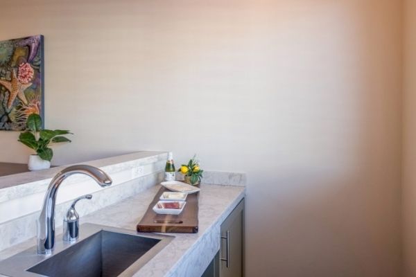 A kitchen counter with a sink, plant, wall art, and utensils on a wooden board.