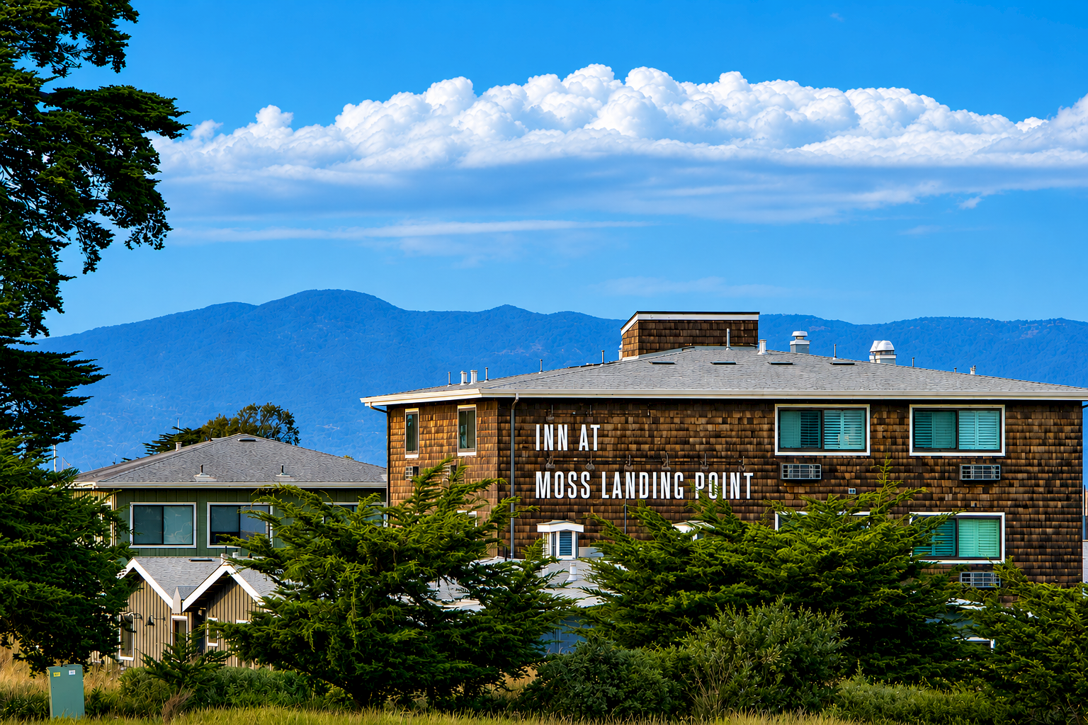 A brick building with the words Moss Landing Point, surrounded by trees, under a bright blue sky with scattered clouds.