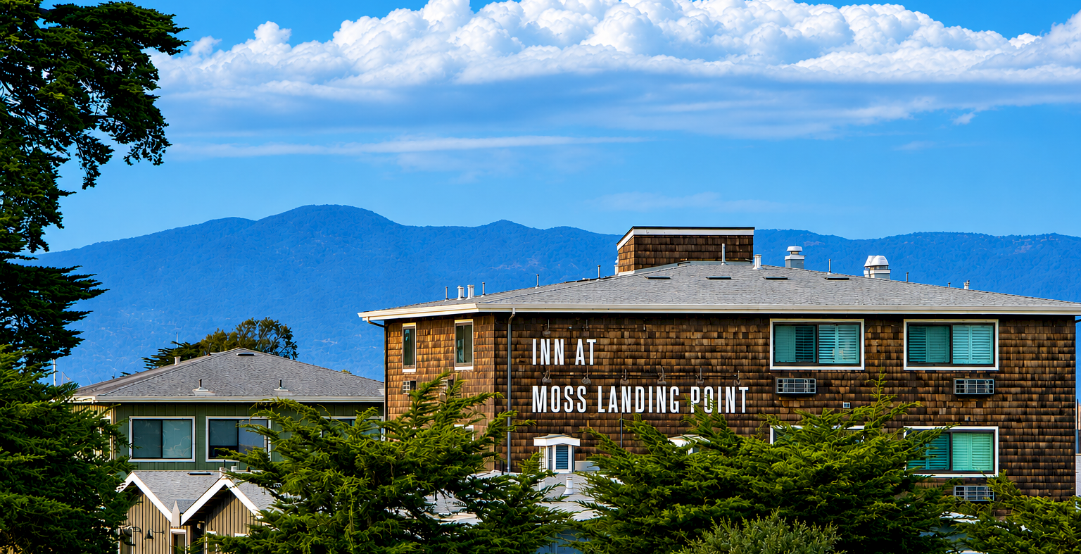 A brick building with the words Moss Landing Point, surrounded by trees, under a bright blue sky with scattered clouds.