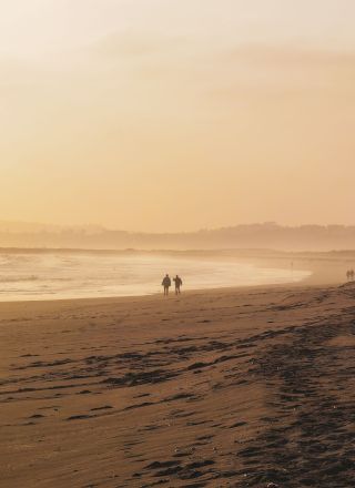 A golden sunrise over a sandy beach with waves rolling in and a few people walking along the shore.