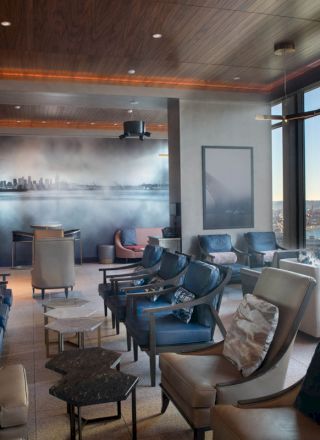 A spacious, modern lounge with leather chairs, large windows offering a scenic view, and a mural of a city skyline on the far wall, ending the sentence.