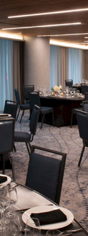 Elegant dining area with round tables set for a meal with plates, glasses, and napkins. The room is well-lit with modern lighting.