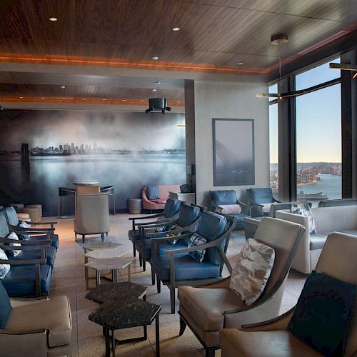 A modern lounge with leather chairs, artwork, and large windows offering a scenic view of a waterfront and a Ferris wheel.