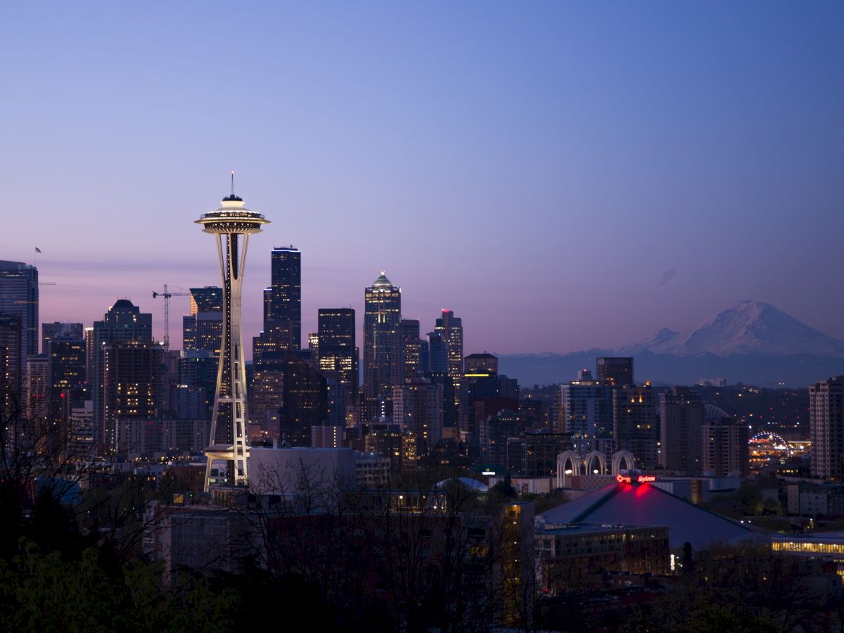 The image showcases the Seattle skyline at dusk, featuring the Space Needle prominently, with Mount Rainier visible in the background.