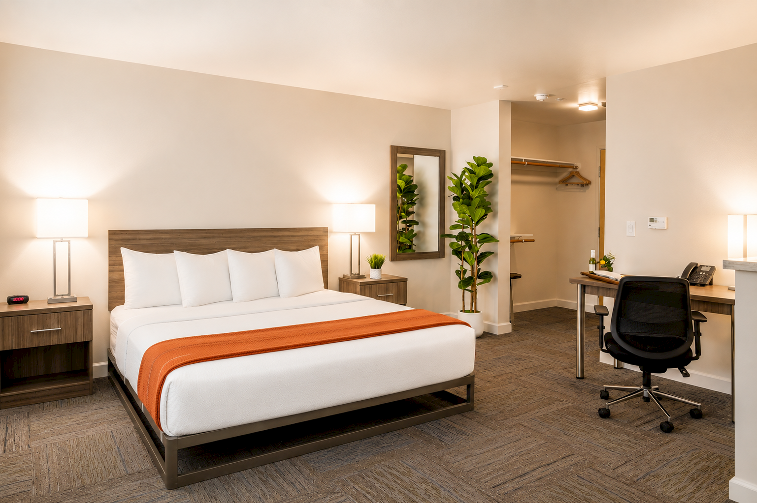 A modern hotel room with a king bed, lamps, wooden headboard, desk with chair, and potted plants.